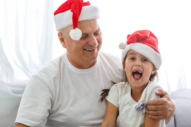 Зворотний портрет радісної дівчинки, яка обіймає дідуся в головних уборах. дідусь і внучка у капелюхах Санта - Клауса. - Фото, зображення