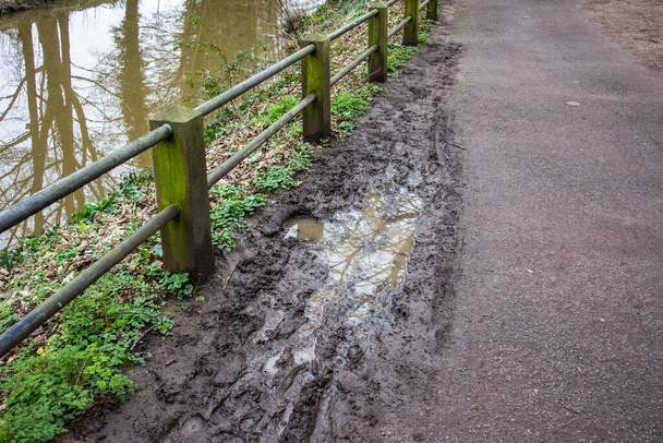 Een modderige plas met voetafdrukken en fietssporen naast een voetpad langs de rivier de Frome In Frome Somerset - Foto, afbeelding
