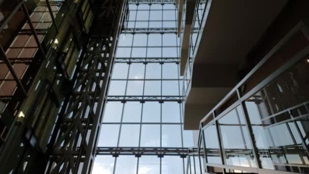 Zaman atlamalı asansör, cam duvarın arkasında beyaz bulutlar yüzen modern şirket binasında hareket ediyor. - Video, Çekim