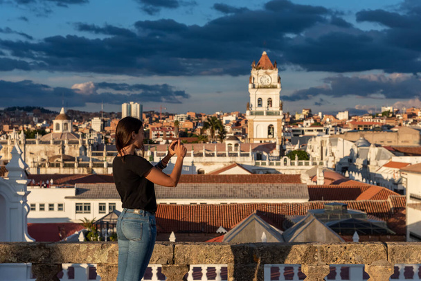 Женщина фотографирует вид на Сукре и его колокольню с крыши в Сукре, Боливия - Фото, изображение