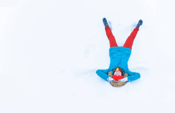 Vue en angle élevé de fille heureuse couchée sur la neige et déplaçant ses bras et ses jambes de haut en bas créant une figure d'ange de la neige. Femme souriante couchée sur la neige en vacances d'hiver avec espace de copie - Photo, image