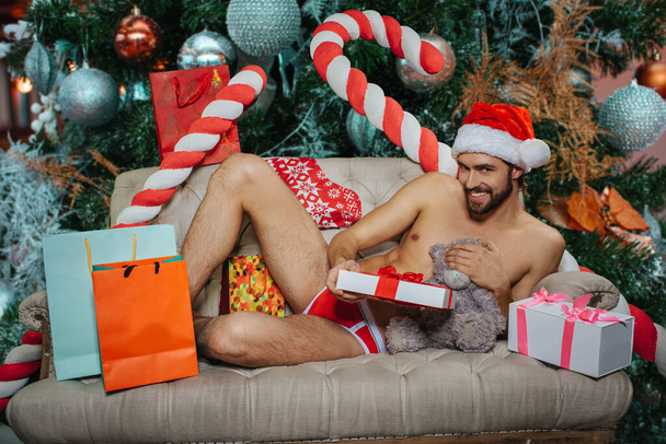 Man in underwear and red hat laying on sofa with gift boxes - Fotoğraf, Görsel