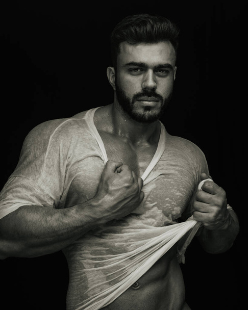 Портрет красивого мужчины-тренажера, держащего мокрую футболку сепией - Фото, изображение