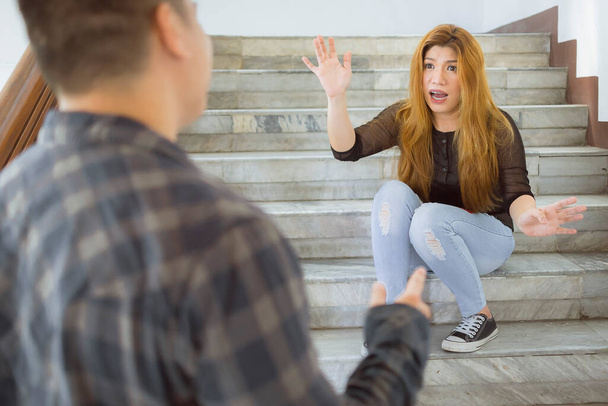 Μια Ασιάτισσα διαφωνεί με τον άντρα της ενώ κάθεται στις σκάλες. Οικογενειακό πρόβλημα, προβλήματα σχέσης ή καυγάδες.. - Φωτογραφία, εικόνα