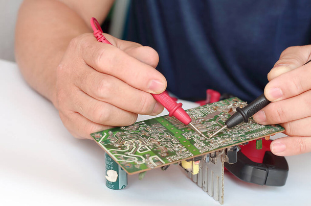 Close up of male hands repairing of electronic, circuit board with multimeter tester. - Photo, Image