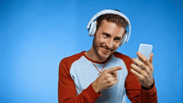 boldog ember vezeték nélküli fejhallgató mutató ujját a telefon kék - Fotó, kép