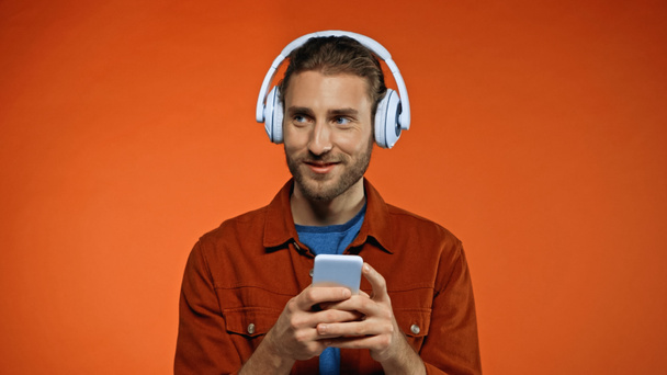 joyful young man in wireless headphones using smartphone on orange  - Фото, изображение