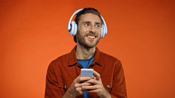 pleased young man in wireless headphones using smartphone on orange  - Fotó, kép