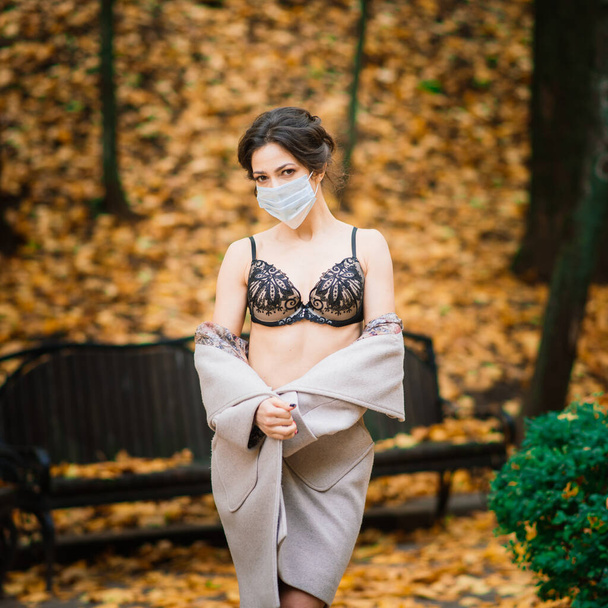 Retrato de moda de mulher sexy em máscara facial e lingerie no parque de outono. Pandemia, vírus, coronavírus - Foto, Imagem