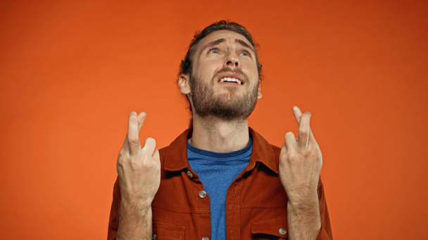 vousatý mladý muž se zkříženými prsty hledící na oranžovou  - Fotografie, Obrázek