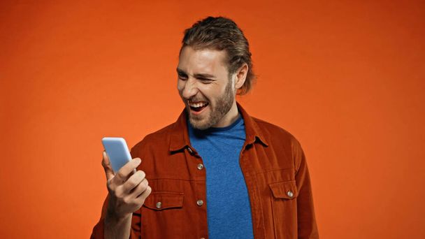 excited bearded man using mobile phone on orange background  - Foto, Imagen