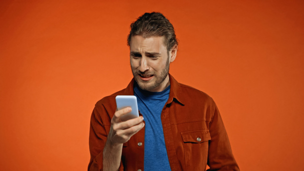 sad young man using mobile phone on orange - Photo, Image