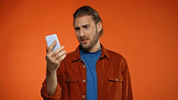 dissatisfied young man looking at mobile phone on orange  - Photo, Image