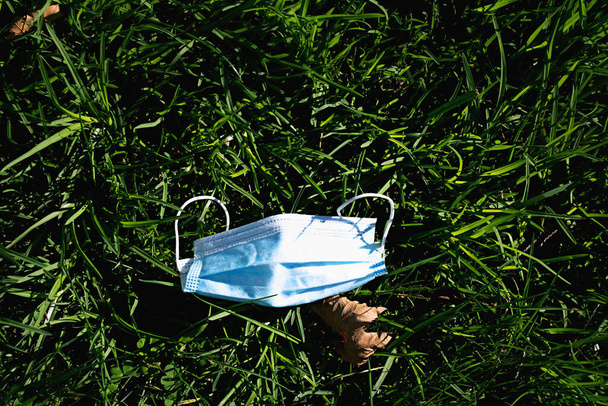 Использованная маска на траве в парке. Новая нормальная концепция. Загрязнение окружающей среды. - Фото, изображение