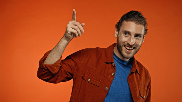 positive young and bearded man smiling while pointing with finger on orange  - Фото, зображення