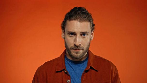 serious bearded man looking at camera on orange background  - Foto, imagen