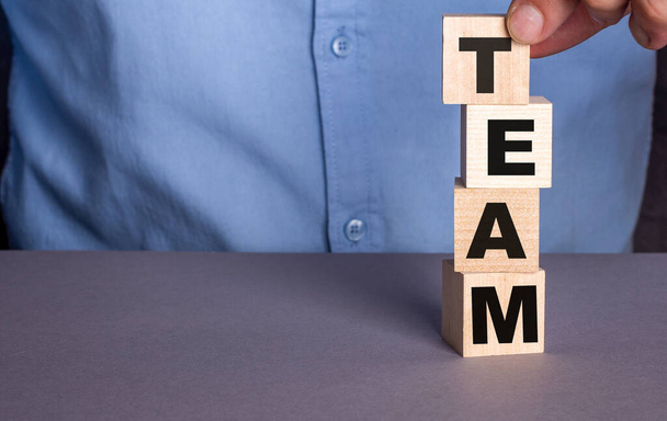 A man in a blue shirt composes the word TEAM from wooden cubes vertically - Φωτογραφία, εικόνα