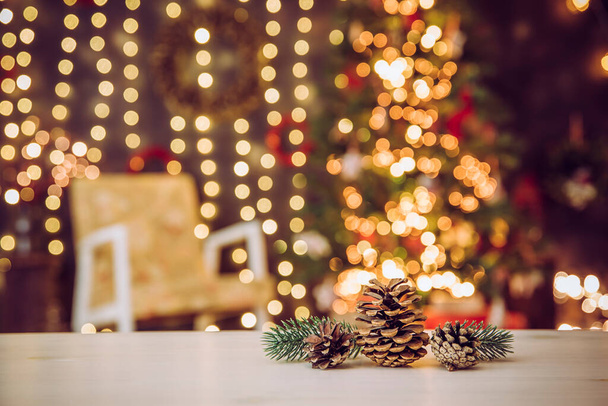  Çam kozalakları, süslü Noel ağacı ve sandalyeli bulanık oturma odası. Bir sürü peri ışığı yanıyor. Noel temalı ürünler veya tebrik kartı arkaplanı, bir sürü kopya alanı. - Fotoğraf, Görsel