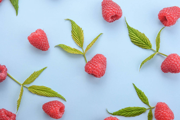 Pattern of raspberry and green leaves on blue background. Flat lay summer berries - red raspberries. Creative minimalism. - Фото, изображение