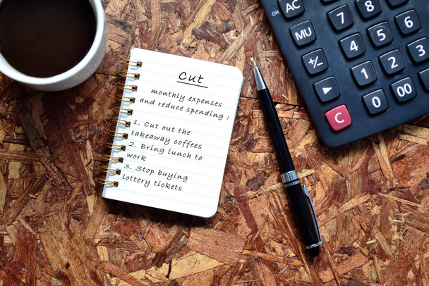 Text written on note pad with background of cup of coffee ,a pen and calculator. Reduce Monthly Expenses Concept.  - Photo, Image