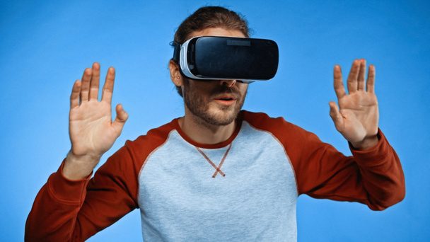 young man in virtual reality headset gesturing on blue  - 写真・画像
