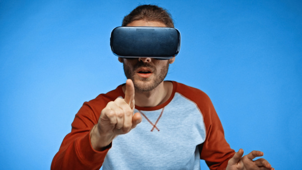 bearded young man in virtual reality headset pointing with finger on blue  - Φωτογραφία, εικόνα
