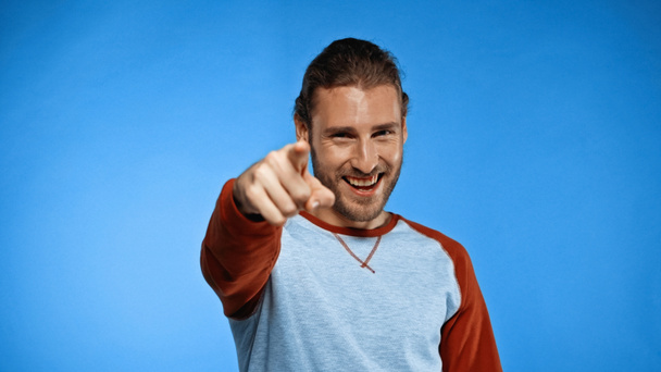 smiling young man pointing with finger while looking at camera on blue - Foto, Bild