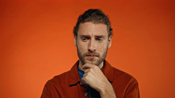 thoughtful man touching beard on orange background  - Foto, Bild