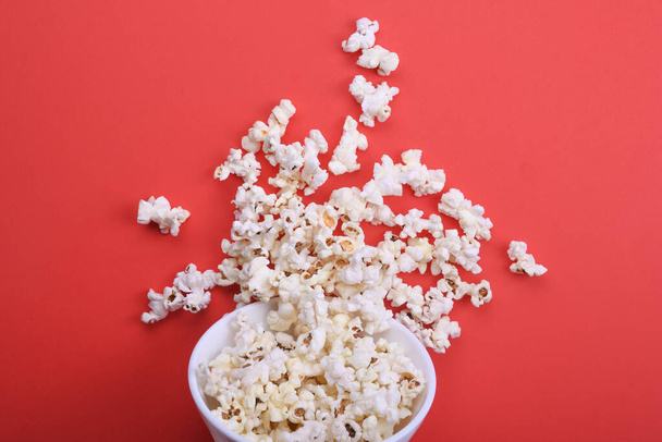 Popcorn pouring from a bowl on a red background. View from above. - Фото, зображення