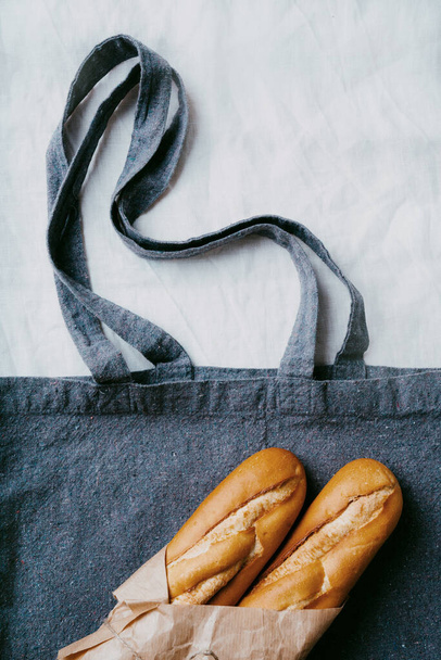 baguette tradizionale francese su fondo tessile blu riciclato avvolto in carta marrone con foglia d'acero. Concetto di pacchetto sostenibile zero rifiuti. Piatto. Vista dall'alto - Foto, immagini
