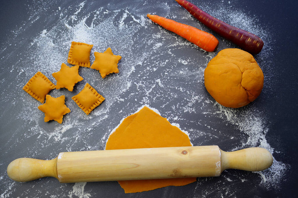Raviolis orange cru en forme de rectangles et étoiles, pâte, carotte et rouleau à pâtisserie sur un fond de farine éparpillée. Le processus de fabrication de raviolis faits maison. - Photo, image