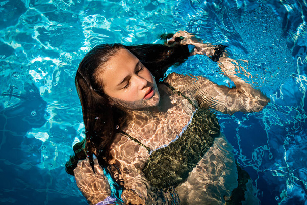 Fashion portret van sierlijk schattig meisje poseren in het zwembad tijdens de vakantie op luxe resort. Vrolijk tienermeisje dat geniet. vrolijke, positieve emotie, zomerse stijl. - Foto, afbeelding