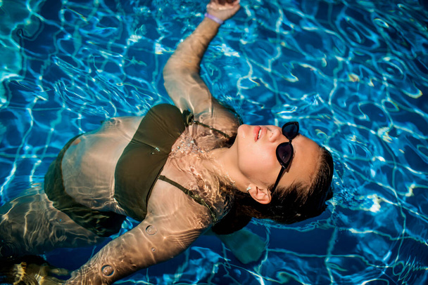 Retrato de moda de la elegante chica linda en gafas de sol elegantes posando en la piscina durante las vacaciones en el complejo de lujo. Alegre más tamaño adolescente disfrutando. feliz, emoción positiva, estilo de verano. - Foto, imagen