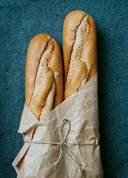 Kahverengi kağıda sarılmış geri dönüşümlü mavi tekstil arkaplan üzerine geleneksel Fransız ekmeği. Sürdürülebilir sıfır atık konsepti. Düz yatıyordu. Üst Görünüm - Fotoğraf, Görsel