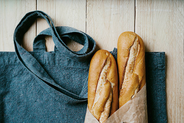 Traditional French baguette over a recycled blue textile bag wrapped in brown paper. Sustainable package zero waste concept. Flat lay. Top View - Photo, Image