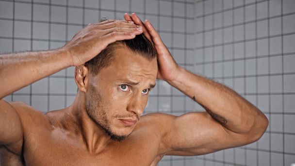 молодой мускулистый мужчина регулирует волосы в ванной комнате  - Фото, изображение