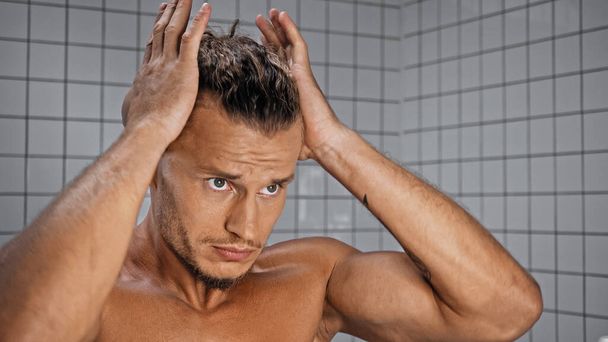 shirtless young man adjusting hair in bathroom  - Photo, Image