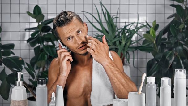 bearded man talking on smartphone in bathroom with plants on blurred background - Fotó, kép
