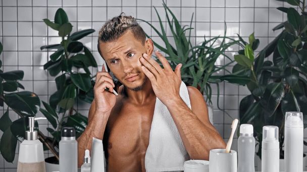 Sakallı adam banyoda akıllı telefondan konuşuyor. Bitkilerin yanında, bulanık arka planda. - Fotoğraf, Görsel
