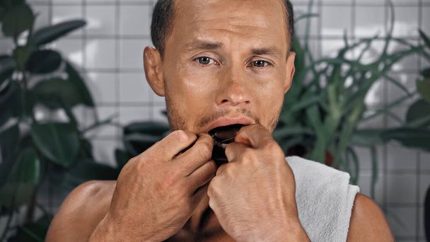 szakállas férfi fogselymezés fogak fürdőszobában növények közelében elmosódott háttér - Fotó, kép