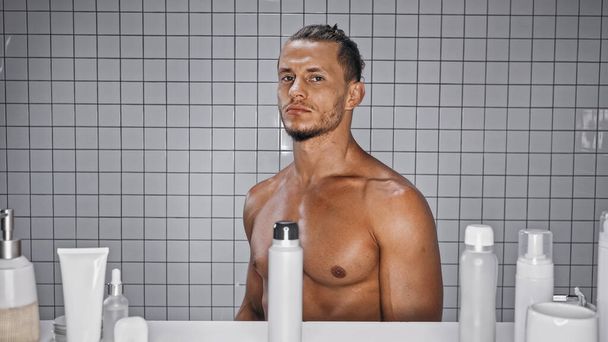 muskulöser Mann steht neben Flaschen im Badezimmer  - Foto, Bild