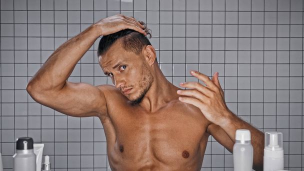 shirtless man adjusting hair near bottles in bathroom  - 写真・画像