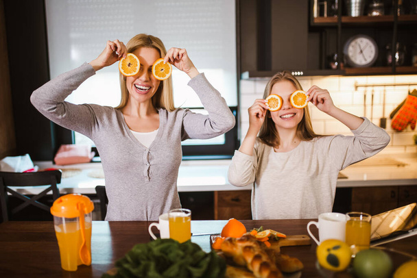 Happy mother and daughter making breakfast at home kitchen and spend time together, having fun with orange - Photo, image