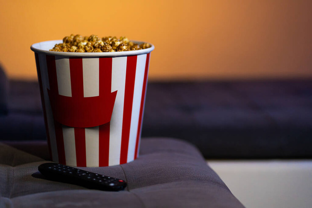A bucket of popcorn on a soft sofa. Time to watch an interesting movie. - Zdjęcie, obraz