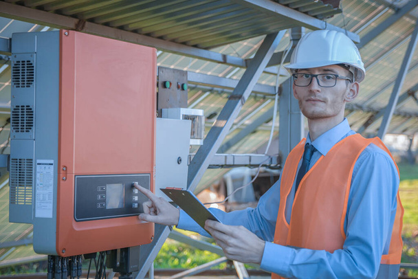 Ingénieur, un homme en uniforme vérifie le système de contrôle de la station solaire sur le fond des panneaux solaires. - Photo, image