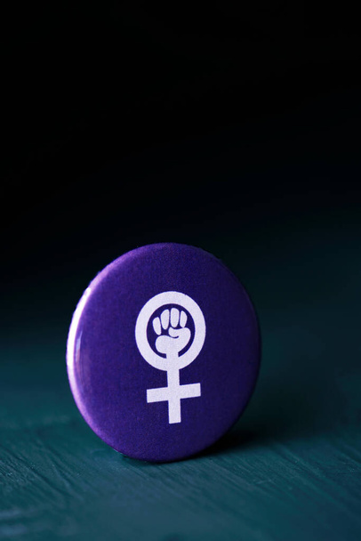 symbol siły kobiet, podniesiona pięść w symbolu płci żeńskiej, w fioletowym przycisku pin na ciemnoszarej powierzchni, na czarnym tle z pustym miejscem na górze - Zdjęcie, obraz