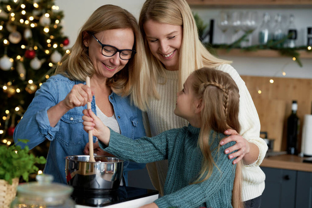 Ευτυχισμένες τρεις γενιές στην κουζίνα κατά τη διάρκεια του ψησίματος των Χριστουγέννων                                - Φωτογραφία, εικόνα