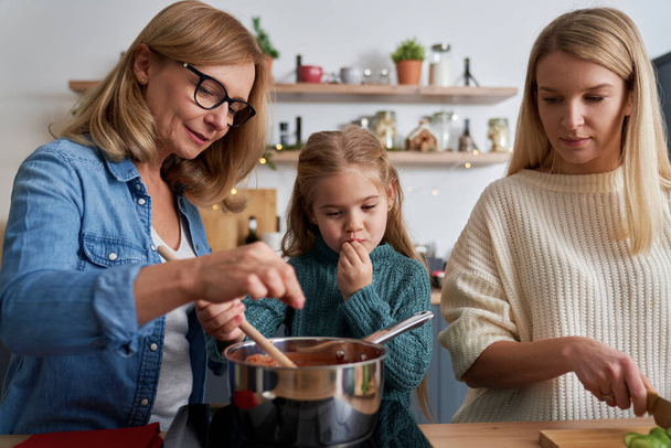 Drei Generationen von Frauen bereiten Essen in der Küche zu                                 - Foto, Bild