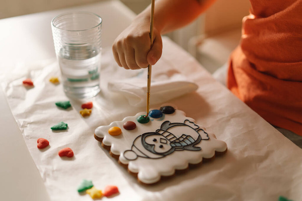 Egy gyerek mázas mézeskalács sütiket fest ételszínezékkel. Kreativitás és hobbik - Fotó, kép