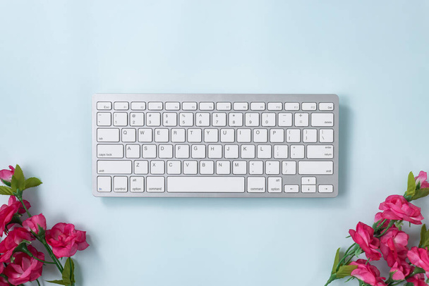 Bílé přenosné klávesnice počítače nebo klávesnice tlačítko a růžový květ v dolní části na modrém pastelovém minimalistickém pozadí - Fotografie, Obrázek